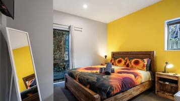 A bedroom with a wooden bed, a nightstand, a mirror, and a window with a view of greenery.