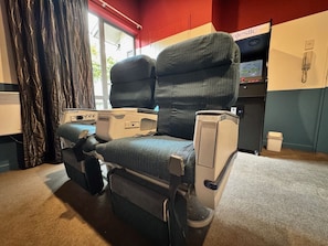 Una habitación compacta con un sillón reclinable, una mesita pequeña, una ventana con cortinas y un mini bar.