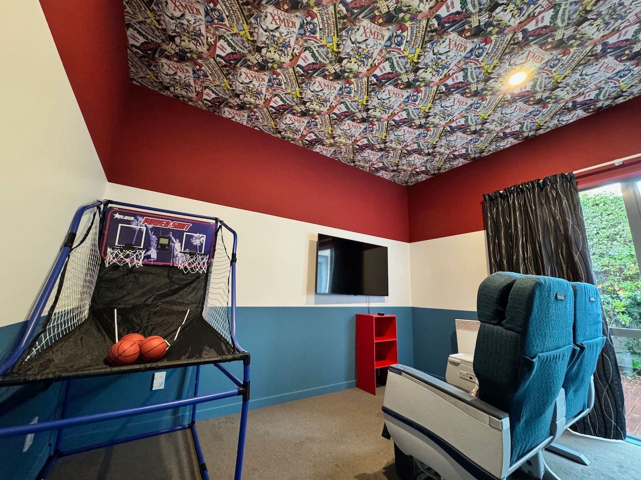 A room with a basketball hoop, a television, and a window with curtains.