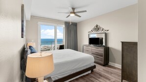 A bedroom with a bed, a TV, a ceiling fan, and a view of the ocean.