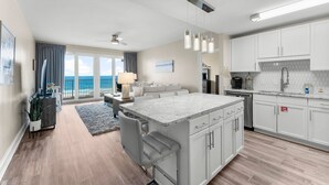 A modern kitchen with white cabinets, a large island, and a view to the outside.