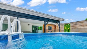 A swimming pool with a white deck and a covered area, surrounded by a wooden fence and a brick building with a 'THANKFUL' sign. - Pool & Canal-View Townhouse | Miami Oasis + BBQ (Miami)