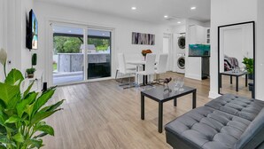 A modern living room with a grey sofa, a dining table with chairs, and a kitchen in the background. - Pool & Canal-View Townhouse | Miami Oasis + BBQ (Miami)