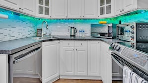 A kitchen with white cabinets, a black countertop, and a backsplash with blue LED lights. - Pool & Canal-View Townhouse | Miami Oasis + BBQ (Miami)