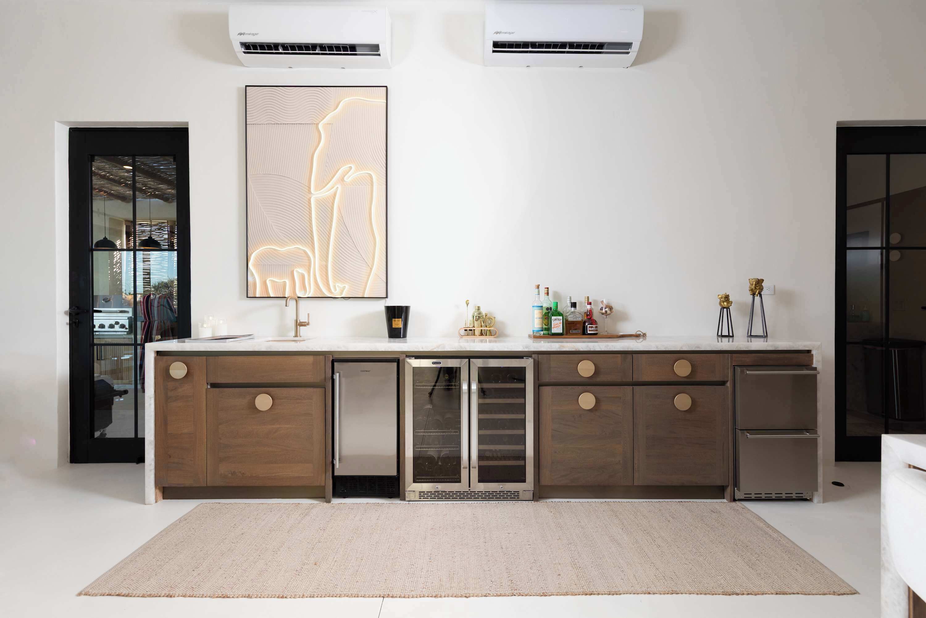 A modern kitchen with a built-in refrigerator, a large illuminated artwork, and a countertop with various items.