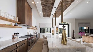A modern kitchen with wooden cabinets, a marble island, and a large window.