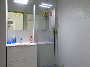 Casa de banho com lavatório branco, espelho e cabine de duche em vidro.