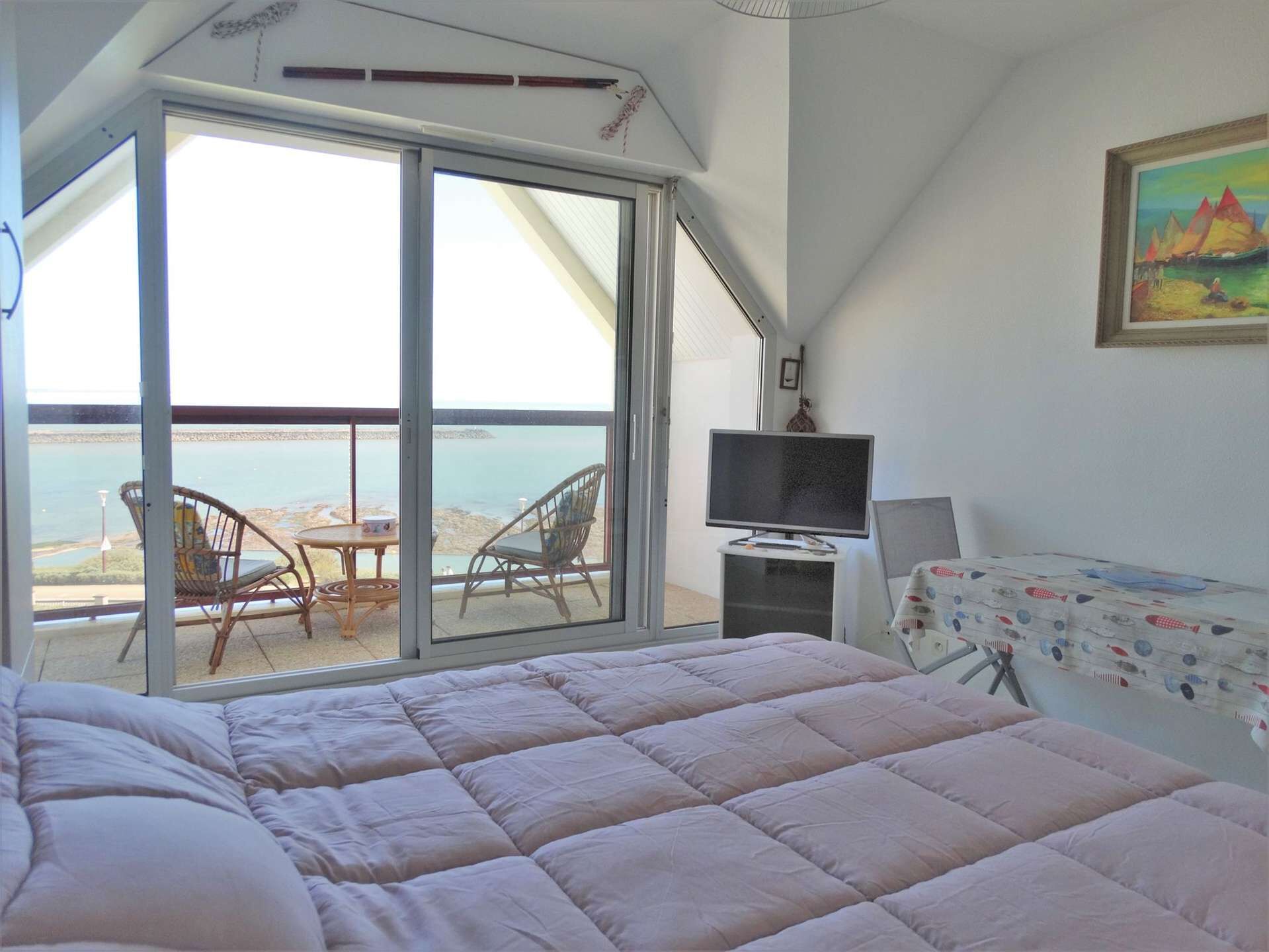 Et soveværelse med en stor seng, et fjernsyn og en balkon med stole og bord med udsigt over vandet.