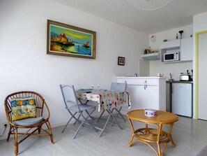 Espaço compacto com mesa de jantar, duas cadeiras, cozinha pequena e um quadro na parede.