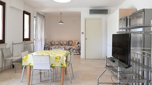 Een eethoek met een tafel voor vier personen, een bank op de achtergrond en een keuken met een koelkast en magnetron.
