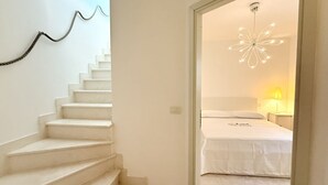 Een trap die leidt naar een slaapkamer met een bed, een nachtkastje, een lamp en een decoratieve plafondlamp.