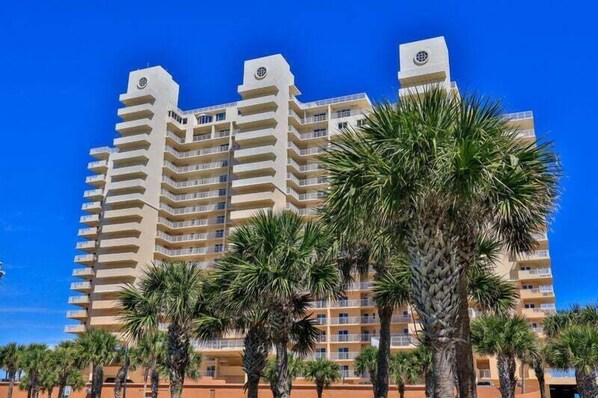 A multi-story hotel with balconies, palm trees in the foreground, and a clear blue sky. - Picturesque Ocean Paradise | Inlet #1206 (New Smyrna Beach)