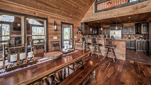 Interior rústico de una cabaña con comedor de madera, chimenea de piedra y cocina con encimeras de piedra.