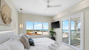 Un dormitorio con cama, ventilador de techo, televisor y vista al mar.