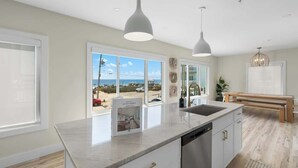 Una cocina moderna con una isla grande, luces colgantes y vistas a la playa.