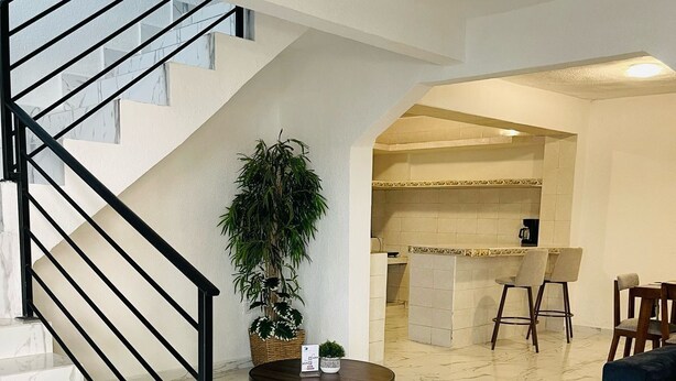 A spacious living area with a marble floor, a staircase with black railings, a round table with a potted plant, and a kitchen area in the background. - Casa Mayor (Tenancingo)
