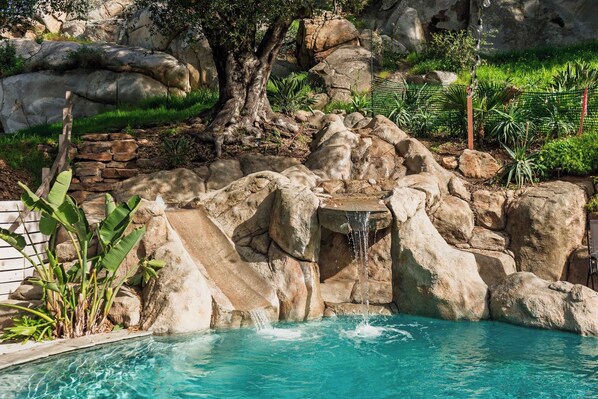 A pool with a waterfall, surrounded by rocks and greenery.