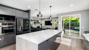 Cozinha moderna com eletrodomésticos de aço inoxidável, uma ilha de mármore e uma porta de vidro corria para um pátio.