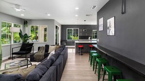 Uma sala de estar moderna com sofá, mesa de centro e televisão. Há também uma área de cozinha com balcão e banquetas.
