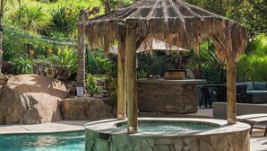 Área de piscina com um bangalô de palha, uma banheira de pedra quente e uma churrasqueira.