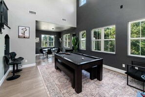 A spacious room with a pool table, a dining area, and large windows.