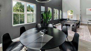 Uma sala de reuniões moderna com uma mesa redonda, cadeiras pretas, mesa de bilhar e janelas amplas.
