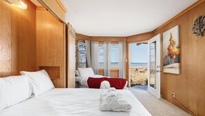 A hotel room with a large bed, a view of the beach, and wooden paneling. - The Tides on East Bay (Traverse City)