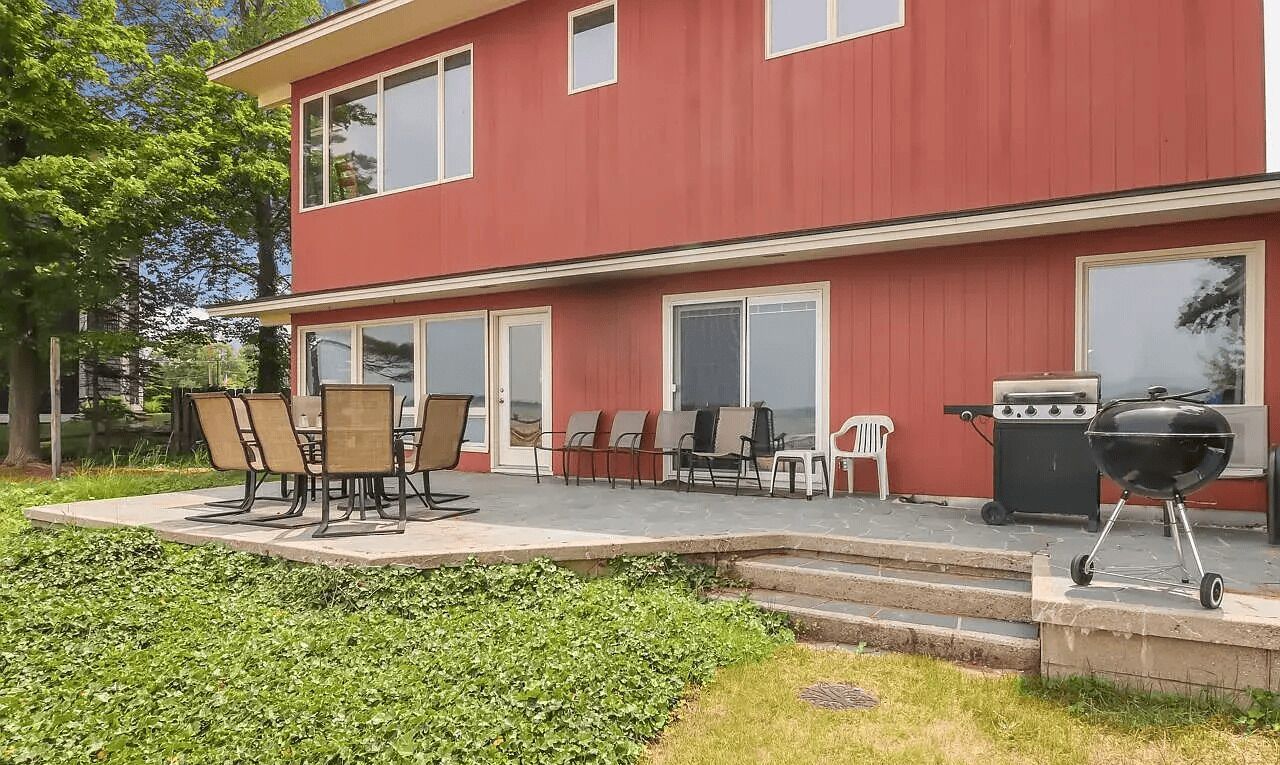 Ett rött hus i två våningar med en uteplats som har ett bord och stolar, en grill och en liten terrass.