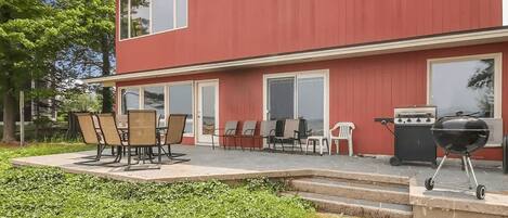 Ett rött hus i två våningar med en uteplats som har ett bord och stolar, en grill och en liten terrass.