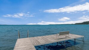 A wooden dock extending into a calm body of water with a bench on it. - The Tides on East Bay (Traverse City)