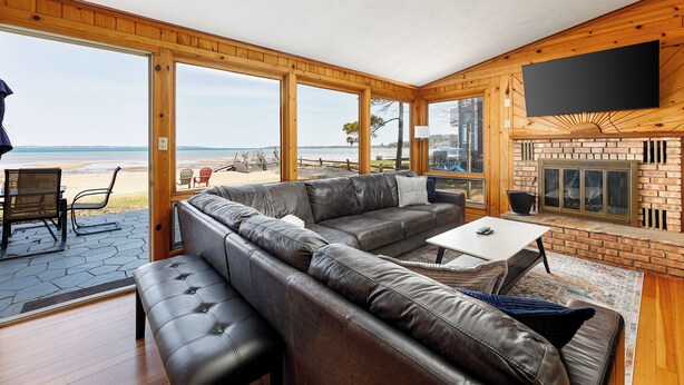 A spacious living room with a large leather sofa, a flat-screen TV mounted on the wall, and a fireplace. - The Tides on East Bay (Traverse City)