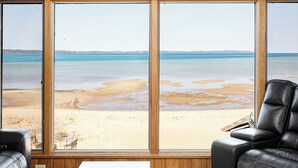 A room with large windows offering a view of a beach and ocean. - The Tides on East Bay (Traverse City)