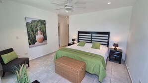 A bedroom with a bed, nightstands, a chair, a ceiling fan, and a large cactus painting. - Two-bedroom ocean view apartment with private pool near hotel facilities (Boca Chica)