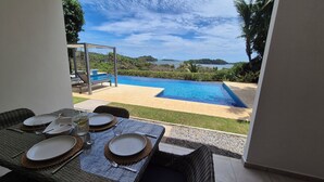 A dining area with a view of a swimming pool and hills in the background. - Two-bedroom ocean view apartment with private pool near hotel facilities (Boca Chica)