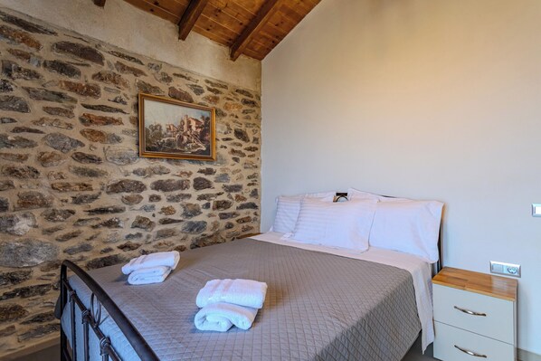 Een slaapkamer met een stenen muur, een bed met witte lakens en een nachtkastje met lades.