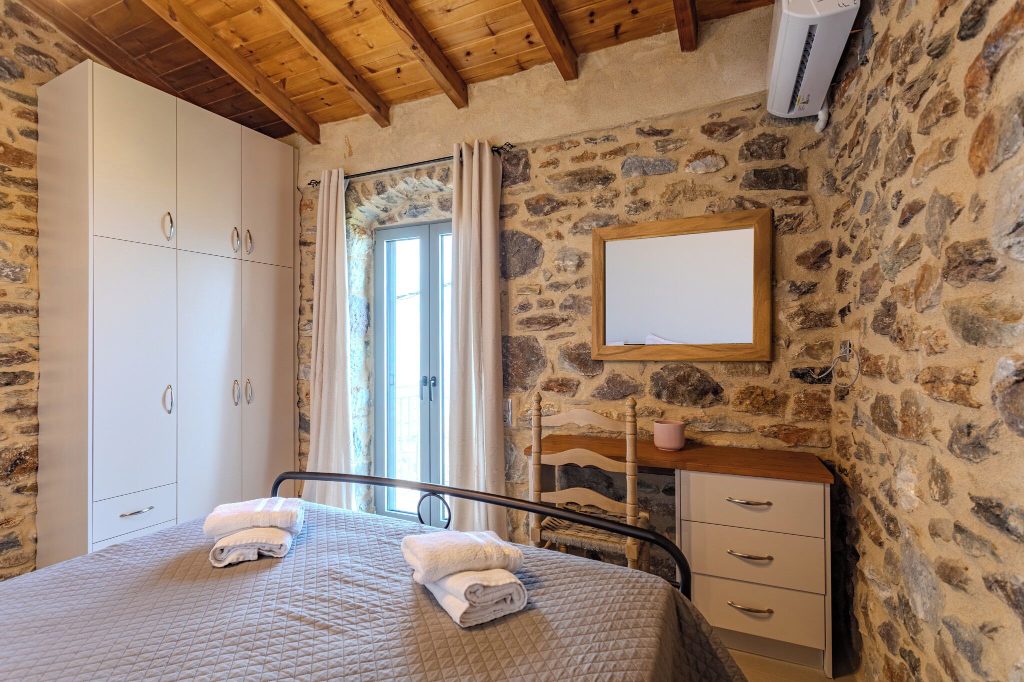 Ett sovrum med en säng, en garderob, en byrå, en spegel och en vägg av sten.