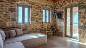 A stone-walled room with a sofa, a chair, a TV, and a sliding glass door. - Charming 2-bedroom apartment with WiFi, AC in lovely Nomitsi (Nomitsi)
