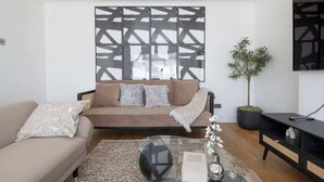 Ein Wohnzimmer mit Sofa, Couchtisch, Topfpflanze und Wand mit geometrischem Muster.