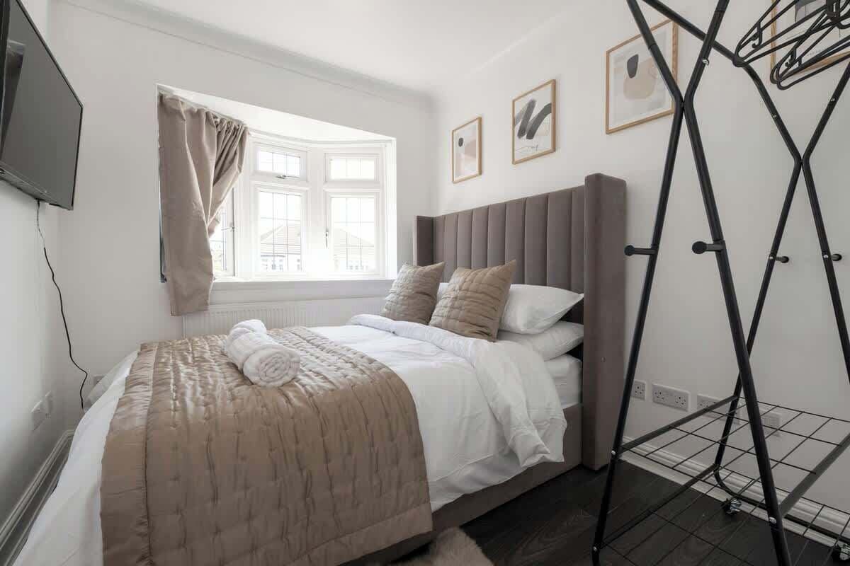 A bedroom with a bed, a window with curtains, a wall-mounted TV, and a metal drying rack.