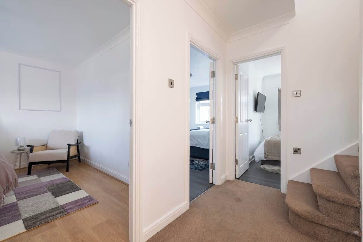 A hallway with a chair, a rug, and a staircase.