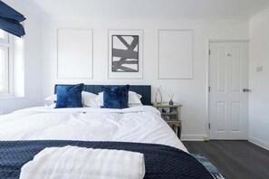 Quarto com cama, mesa de cabeceira, porta e quadros na parede.