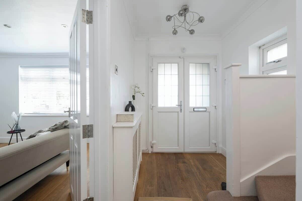 Un couloir avec une porte blanche, un escalier et un luminaire au plafond.