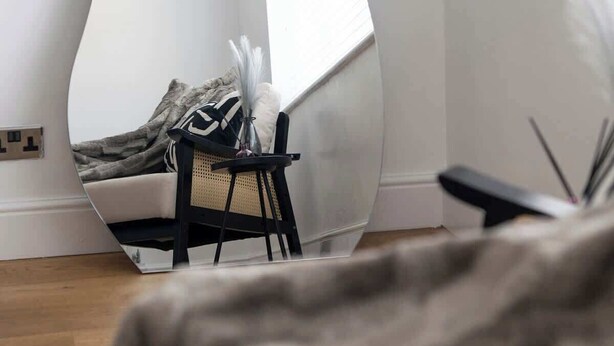 Ein modernes Zimmer mit einem einzigartigen, gebogenen Spiegel, einem kleinen schwarzen Stuhl und einer dekorativen Vase.