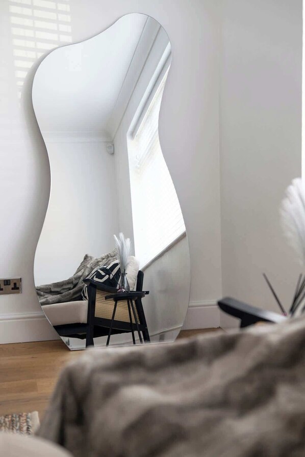 Una habitación moderna con un espejo curvo original, una pequeña silla negra y un jarrón decorativo.