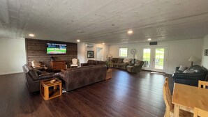 A spacious living room with a large sectional sofa, a wooden coffee table, and a TV mounted on the wall. - Timberside - A Getaway for the Whole Group (Dyersville)