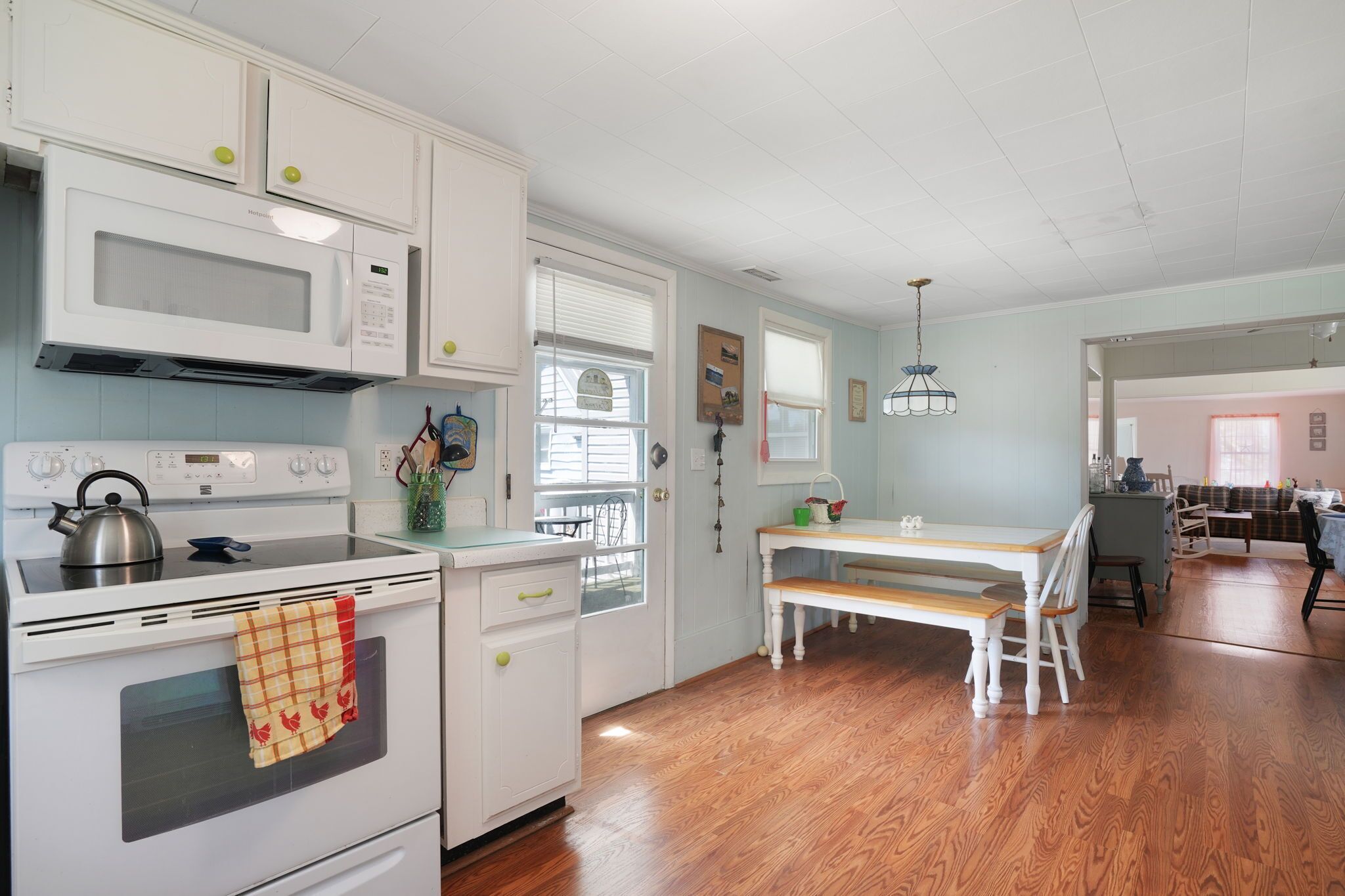 A kitchen with white cabinets, a microwave, stove, and a dining area with a bench and table.
