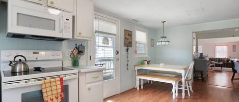 A kitchen with white cabinets, a microwave, stove, and a dining area with a bench and table.