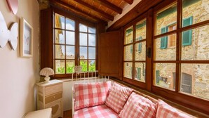 A cozy room with a checkered sofa, a small bedside table with a lamp, and large windows with shutters.