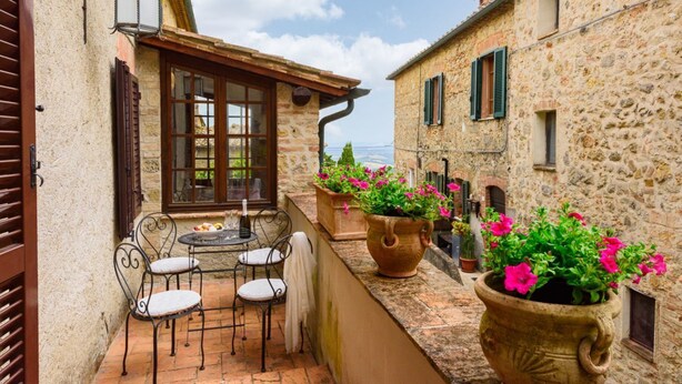 A stone building with a balcony, outdoor seating, and potted plants.