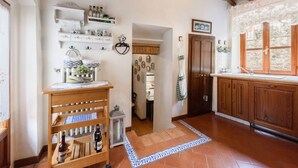 A rustic kitchen with wooden cabinets, a wine rack, and a tiled floor.